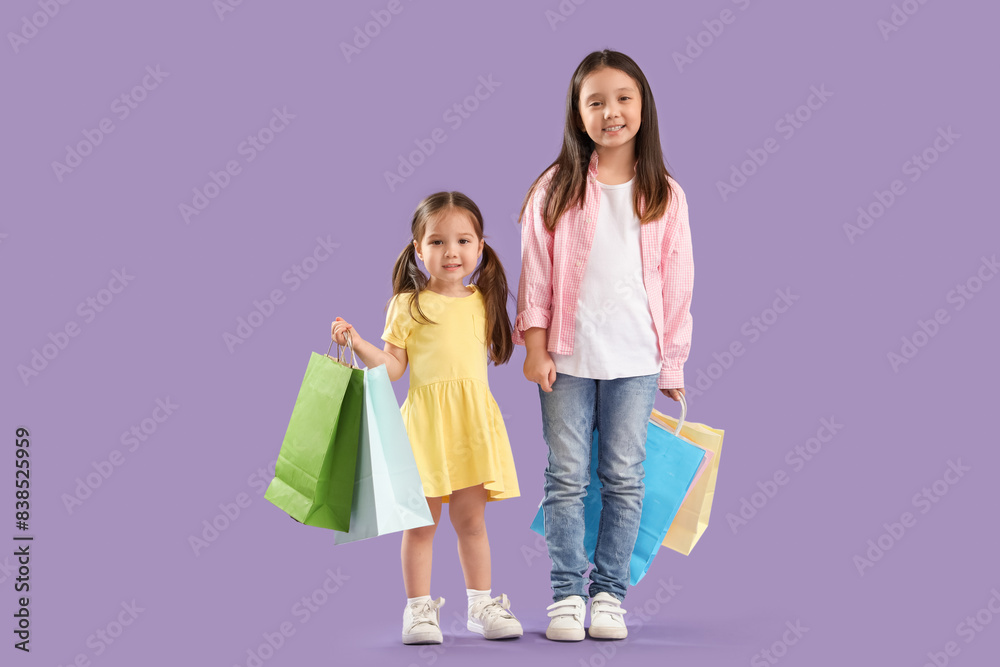 Cute little Asian happy sisters with shopping bags on purple background Cute little Asian happy sisters with shopping bags on purple background
