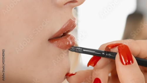 Detailed closeup as a woman meticulously applies lip gloss with a brush, enhancing her beauty. Shiny lips, red nails add sophistication to her makeup routine, showcasing precision and elegance photo