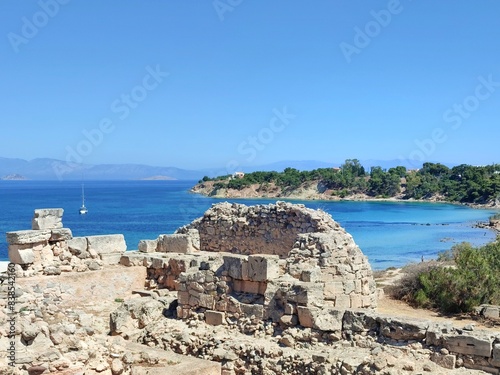 Photo of the Temple of Apollo ruins on Aegina Island, Greece, with Kolona Beach and its crystal-clear waters in the background, offering a stunning blend of ancient history and scenic beauty. photo