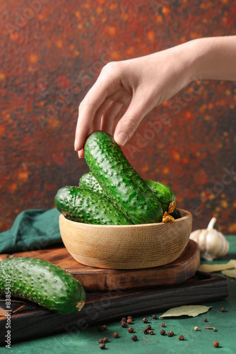 Female hand with wooden bowl of fresh green cucumbers on colorful background photo