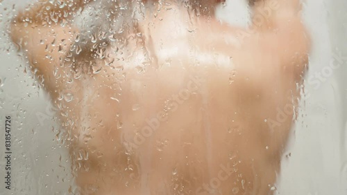 Blurred Silhouette of a Naked Woman in the Shower Cabin Washing Her Long Brown Hair, Water Droplets on the Glass.