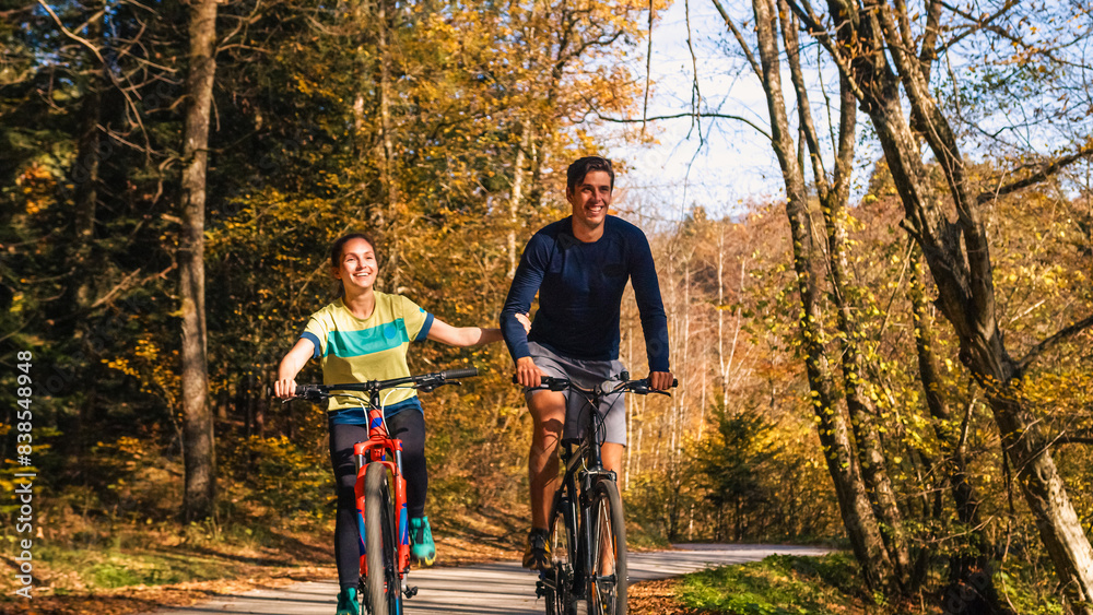 Young happy couple cycling downhill along the autumn forest trail, holding hands and having fun in the ride. Nature, fun, relaxation, and active lifestyles concepts. Young happy couple cycling downhill along the autumn forest trail, holding hands and having fun in the ride. Nature, fun, relaxation, and active lifestyles concepts.