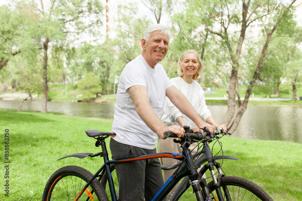 elderly senior couple rides bicycle in the park in the summer and smiles, old gray-haired man and woman are actively resting outdoors, old people practice cycling in forest elderly senior couple rides bicycle in the park in the summer and smiles, old gray-haired man and woman are actively resting outdoors, old people practice cycling in forest