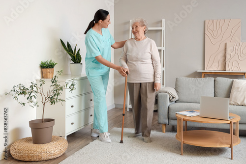 Senior woman with stick and physical therapist walking at home