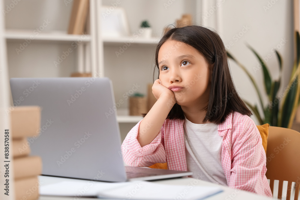 Upset little Asian girl with laptop studying online at home Upset little Asian girl with laptop studying online at home