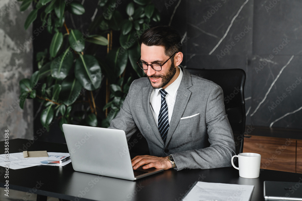 Successful boss typing on laptop remotely in office. Young rich manager businessman checking financial data, doing managerial online job, receiving official letters and e-mails Successful boss typing on laptop remotely in office. Young rich manager businessman checking financial data, doing managerial online job, receiving official letters and e-mails