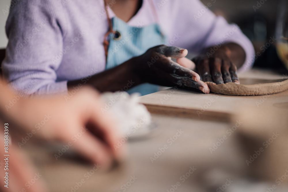 Close up of diverse pottery class attendee's hands making clay plate. Close up of diverse pottery class attendee's hands making clay plate.