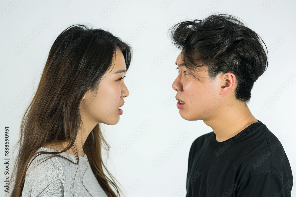 On a stark white background, an Asian young couple stands in tense confrontation, their expressions etched with anger and frustration On a stark white background, an Asian young couple stands in tense confrontation, their expressions etched with anger and frustration