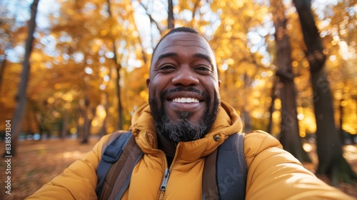 A beaming man with a backpack captures a selfie amid the golden fall foliage