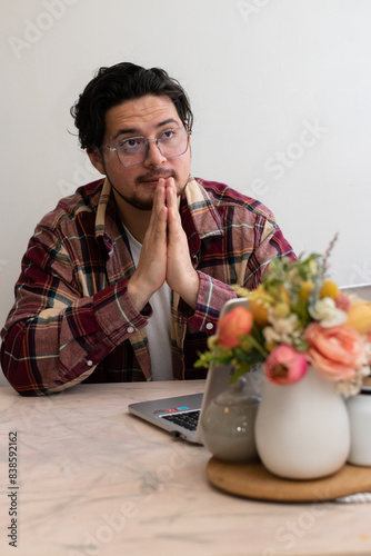Young student praying to god for help to resolve his problems in the living room with laptop