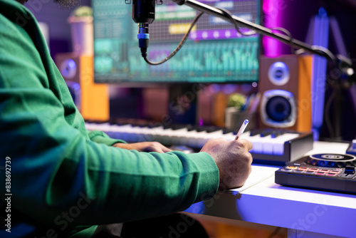 Musician taking notes on paper to produce a new track, making rhymes and blending musical elements together. Producer songwriter composing new melodic verses for a tune. Close up. photo