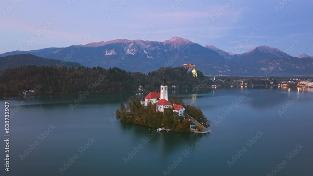 Aerial hyper lapse Bled Island (Blejski otok) with pilgrimage church of the Assumption of Mary and Bled castle on Lake Bled at evening, Slovenia