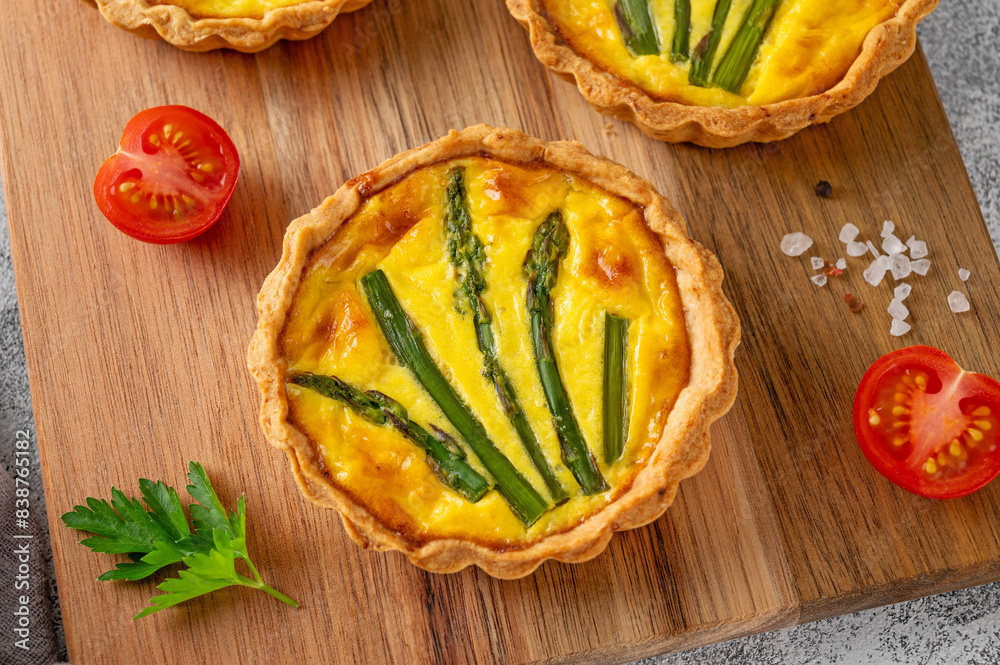 Mini tarts with green asparagus and cheese with cream filling on a wooden board on a light concrete background. Top view, selective focus. Mini tarts with green asparagus and cheese with cream filling on a wooden board on a light concrete background. Top view, selective focus.