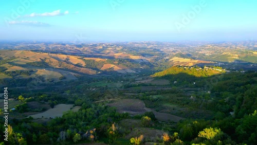 Delicate aerial push-in and pan-left shot from Penna San Giovanni (MC) showing the broad expanses of thickets, fields, meadows, roads and buildings on the outskirts of the town centre under few clouds