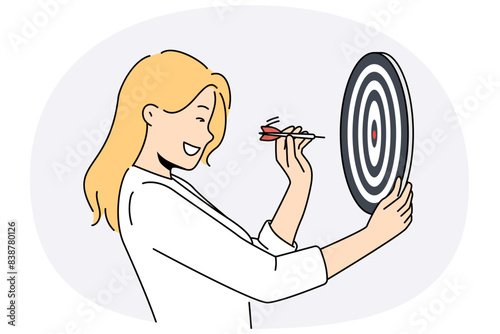 Determined woman throws darts at target for concept of business success and achieving set goals. Goal oriented businesswoman with darts board smiling setting and achieving ambitious goals