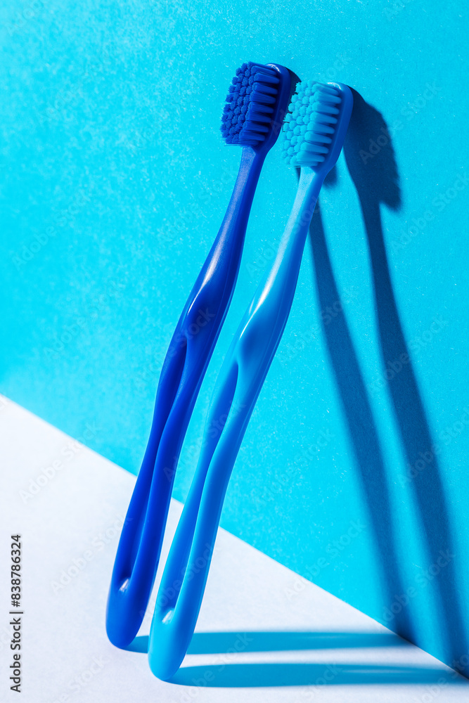 Zwei blaue ergonomisch geformte Zanhbürstn mit dichtem Borstenfeld, stehend an blauer Wand angelehnt Zwei blaue ergonomisch geformte Zanhbürstn mit dichtem Borstenfeld, stehend an blauer Wand angelehnt