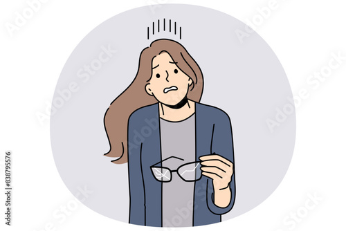 Woman with broken glasses in hands makes confused face not knowing how to solve vision problem. Careless girl holds glasses with cracked glass and needs to go to optometrist or buy contact lenses