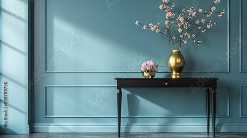 A sleek black lacquered table with a gold vase holding peonies, set against a light blue wall. photo
