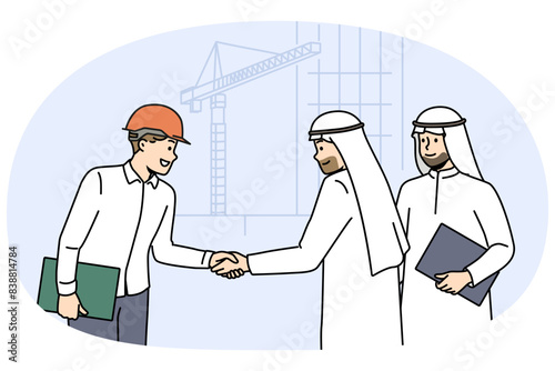 Handshake of arab businessmen and builder from architectural bureau standing near tower crane. Manager of international construction company makes important business deal with arab investors
