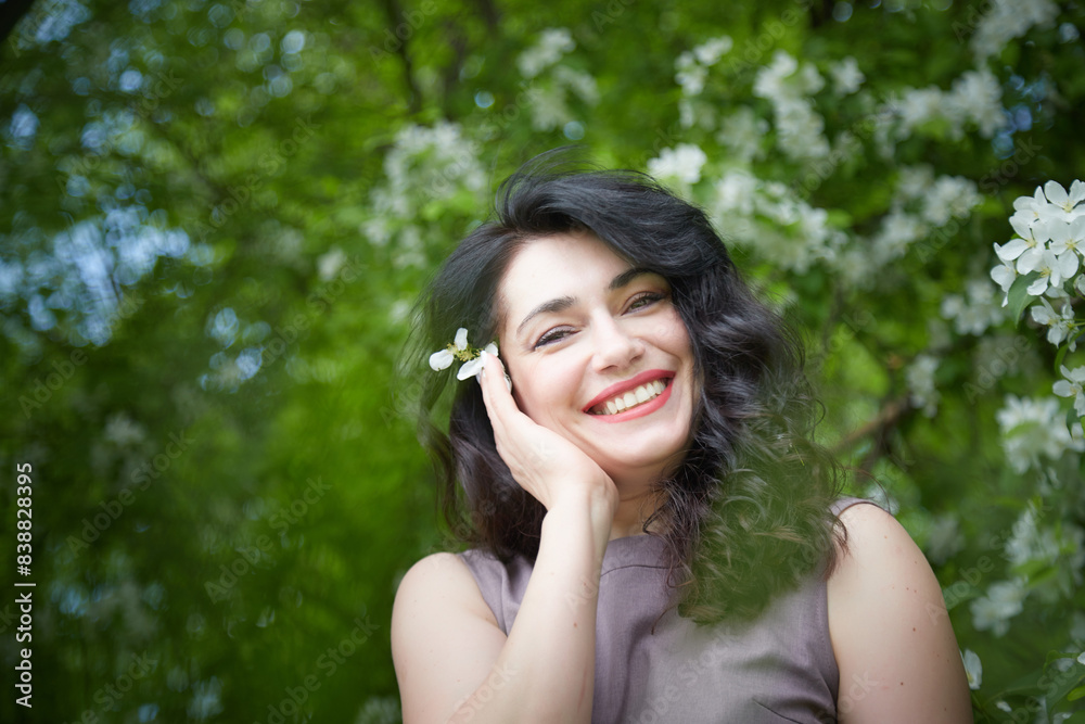 Joyous brunette woman near Blossoms of apple tree in a Spring Garden outdoors. Concept of face and body care. The scent of perfume and tenderness Joyous brunette woman near Blossoms of apple tree in a Spring Garden outdoors. Concept of face and body care. The scent of perfume and tenderness