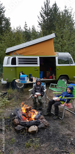 Kids enjoy campfire warmth by a vintage camper van