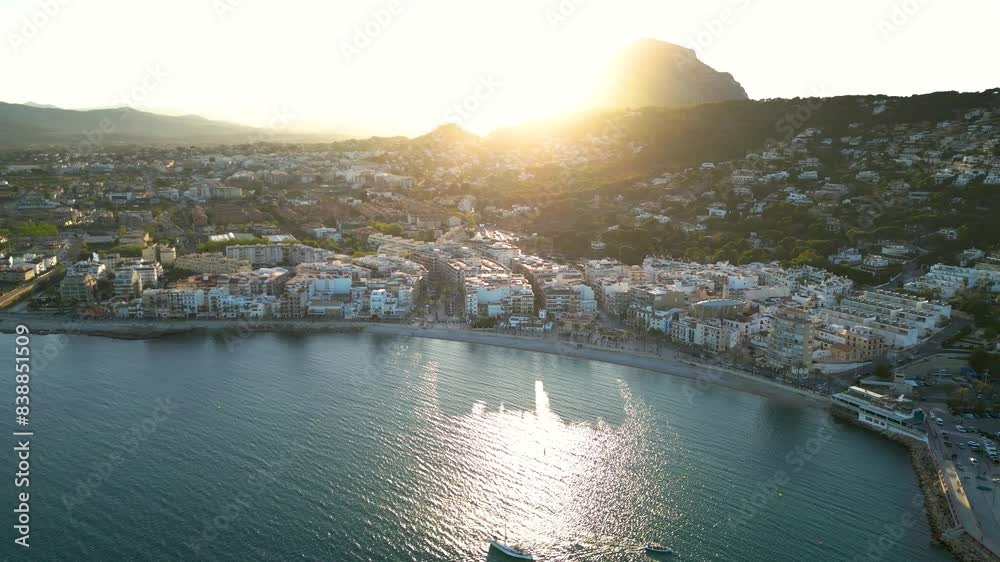 Xabia - Javea - Spain. Panoramic aerial view of the city. Sunet point, the sun sets behind the mountain. Orange sunset. Famous travel destination. Drone going backwards above the bay.