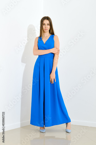 Pretty woman in long blue dress with low neckline on white background, apparel shoot