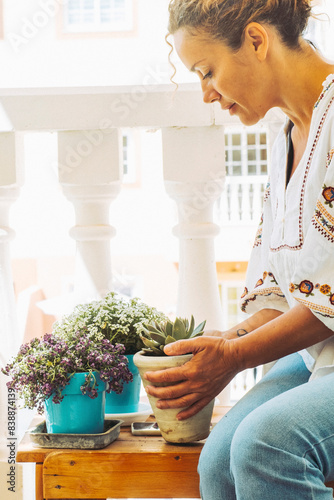 Beautiful lady takes care of her plants on the balcony. Sitting blonde lady admires her flowers. Hobby and botanical care concept