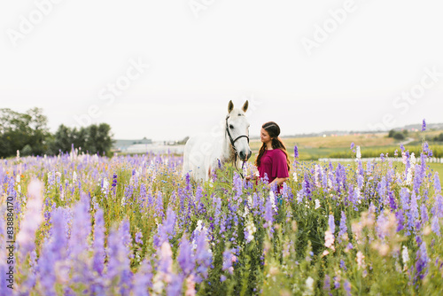 Brunette young girl with grey and white horse in wildflower field photo