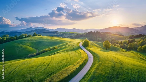 Colorful landscape with curved rural road in green meadows. Aerial view of long winding country road leading through green hills at sunset in summer. Alpine mountains  blue sky with clouds. Slovenia