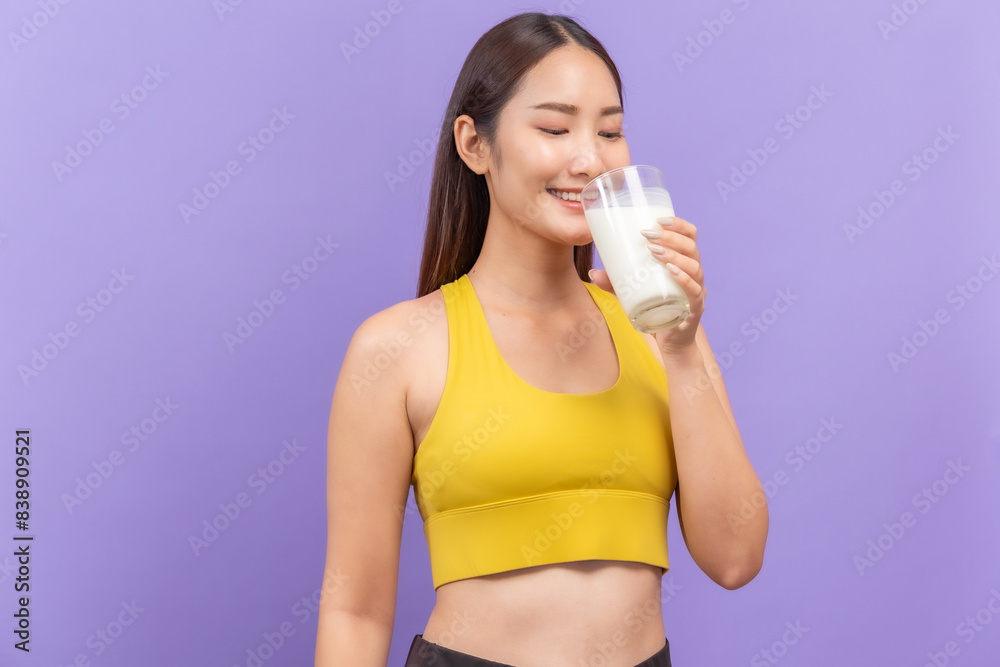 Young woman in a yellow sports bra, joyfully drinking a glass of milk, with a purple backdrop Young woman in a yellow sports bra, joyfully drinking a glass of milk, with a purple backdrop