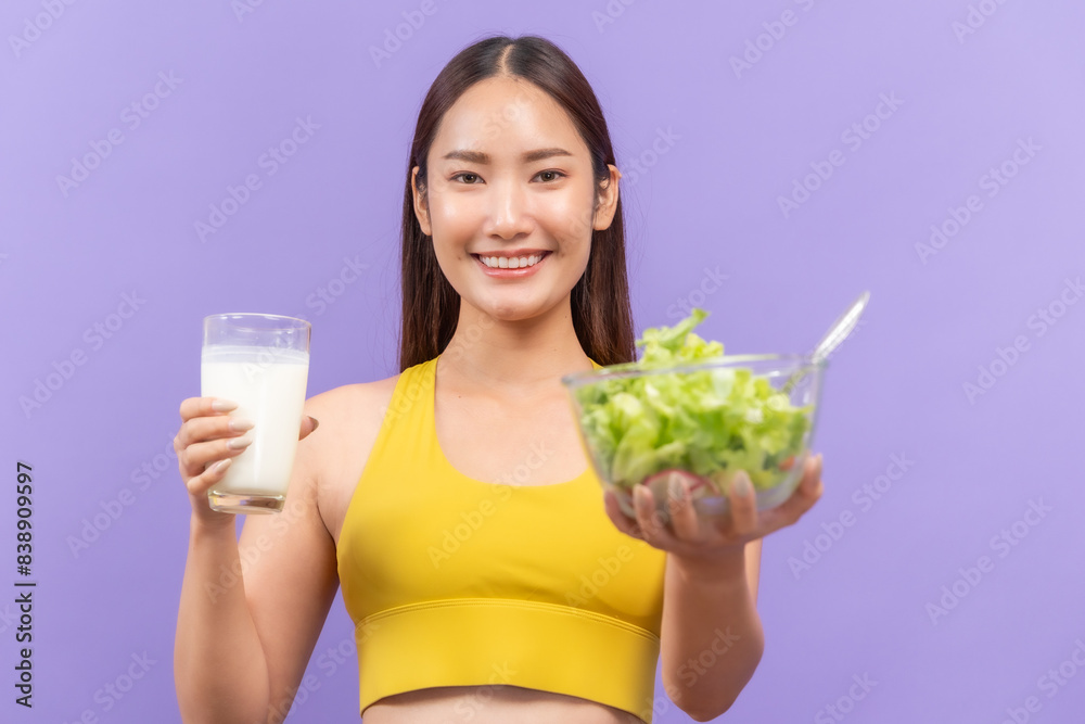 Young woman in a yellow sports bra, joyfully drinking a glass of milk, with a purple backdrop Young woman in a yellow sports bra, joyfully drinking a glass of milk, with a purple backdrop