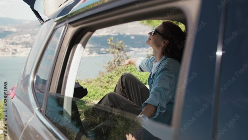 A young woman enjoying a beautiful sea view while sitting in the trunk of her SUV car. A young woman enjoying a beautiful sea view while sitting in the trunk of her SUV car.