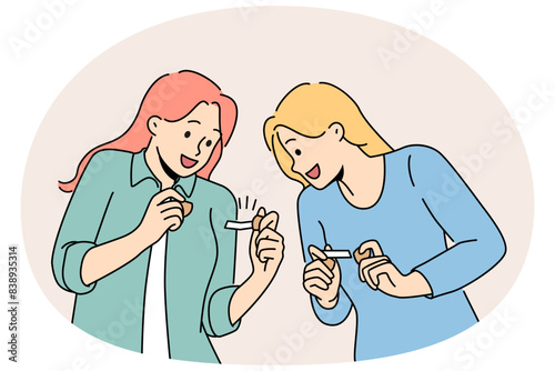Happy girls hold fortune cookies and laugh as rejoice at cheerful wishes found inside pastry. Young women in casual clothes are intrigued reading messages hidden in cookies with wishes.