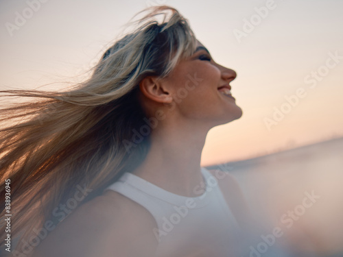 Canvas Print A woman with her hair blowing in the wind during a tranquil sunset, evoking a se