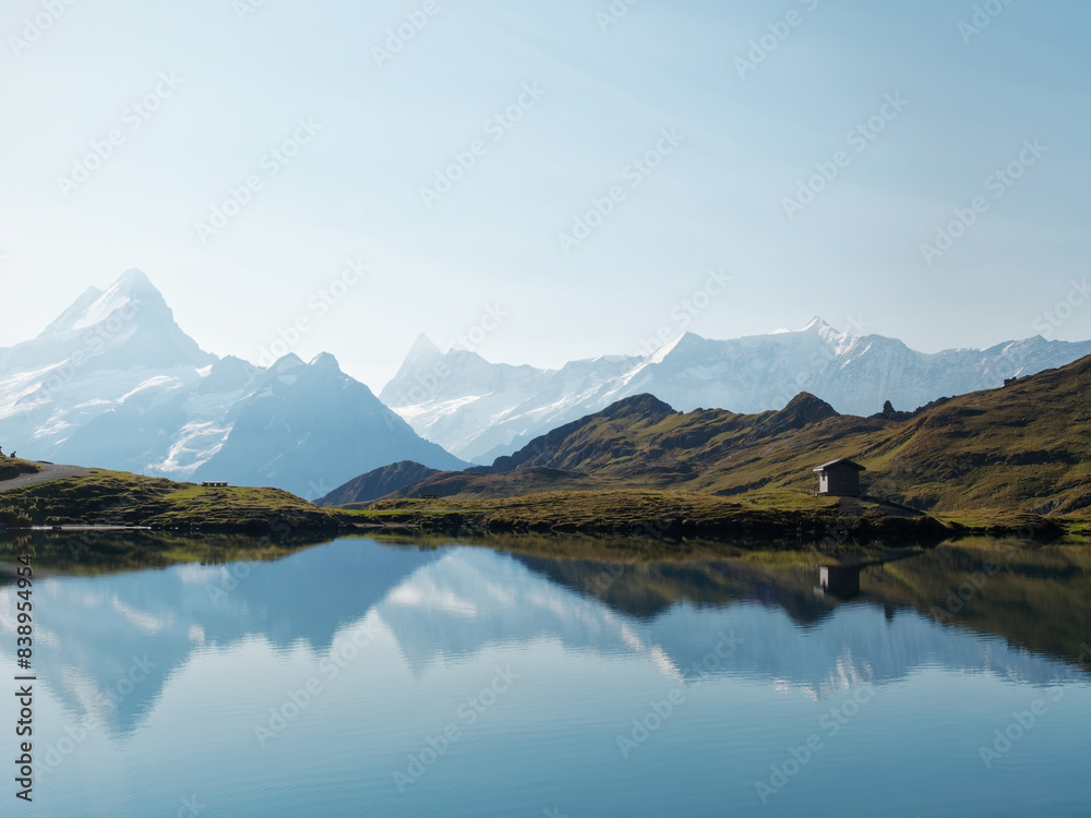 Naklejka premium Scenic Swiss lake with mirrored mountains, a serene wooden cabin on the shore