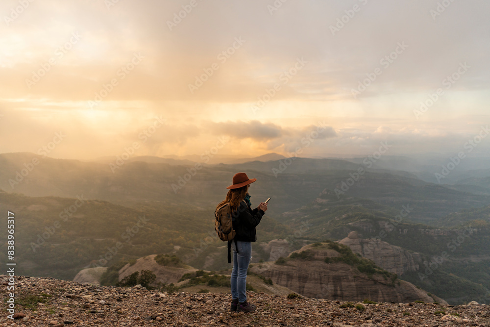 Woman with backback, standing on mountain, looking at view, using smartphone Woman with backback, standing on mountain, looking at view, using smartphone