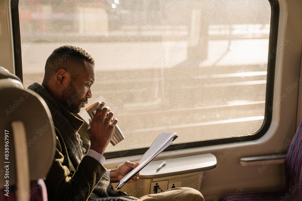 Stylish businessman with reusable cup and documents in a train
