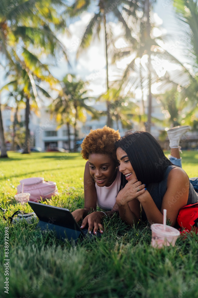 Two happy female friends relaxing in a park using a tablet
