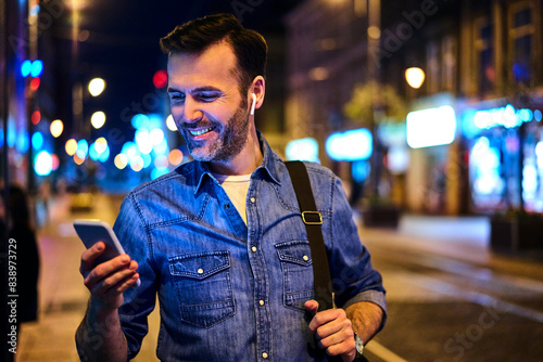 Man with wireless headphones using smartphone in the city at night photo