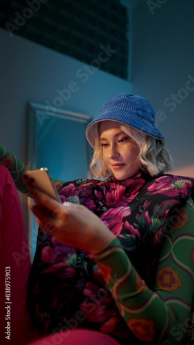 Vertical Trendy stylish woman sitting at armchair and browsing internet on smartphone