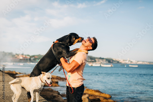 Obraz na płótnie Cheerful man wearing sunglasses playing with dogs at beach against sky w salonie