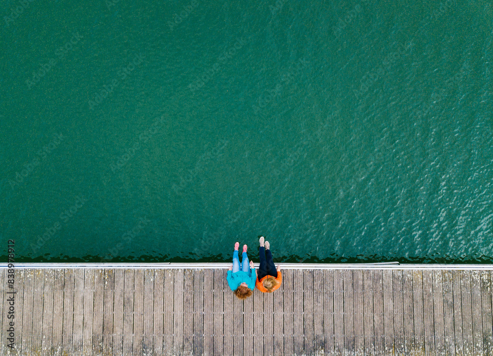 Two friends sitting side by side on jetty, Valdemurio Reservoir, Asturias, Spain