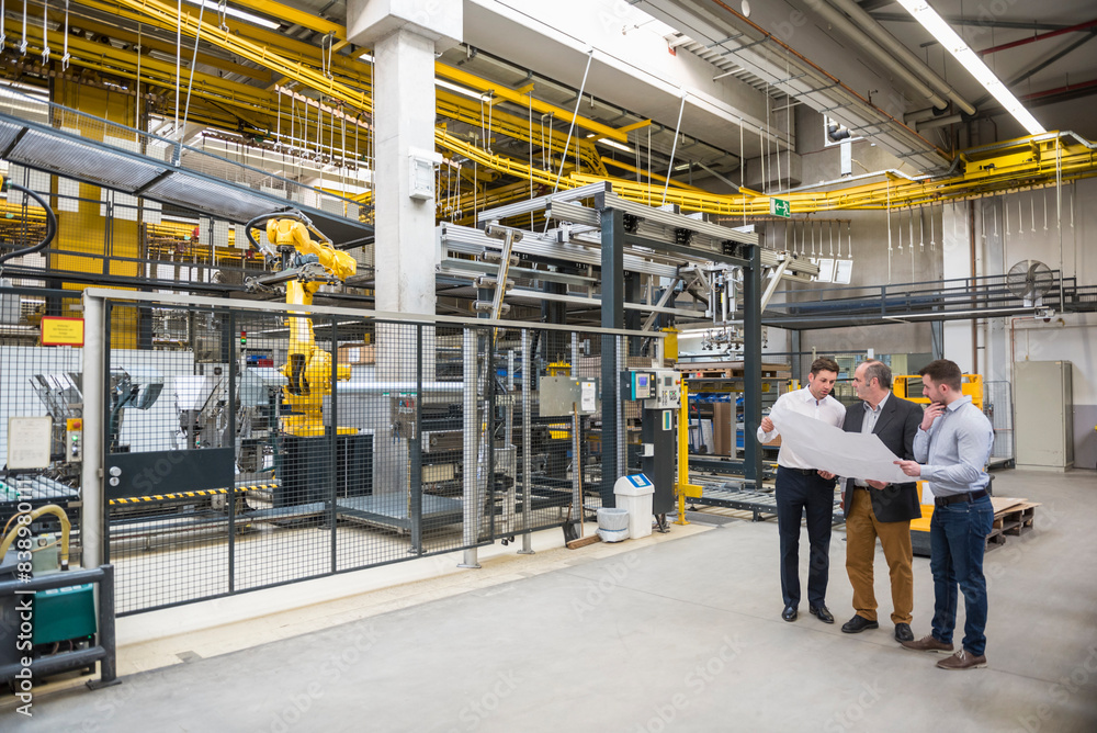 Three men with blueprint talking in factory shop floor