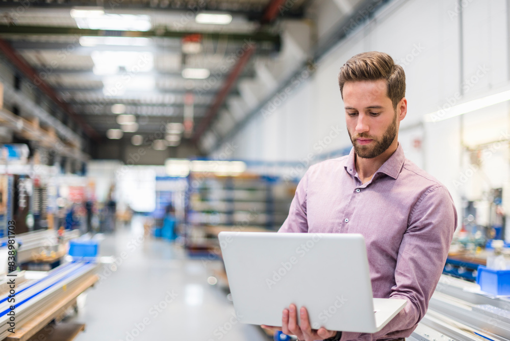 Young businessman using laptop in production hall