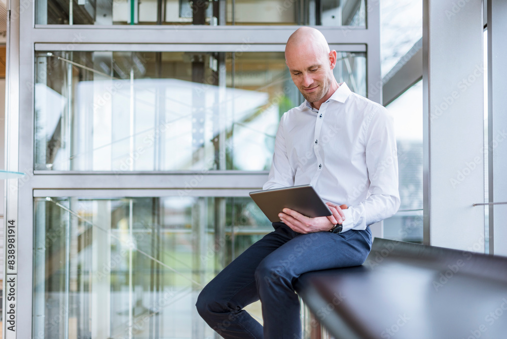 Smiling businessman sitting at the window using tablet
