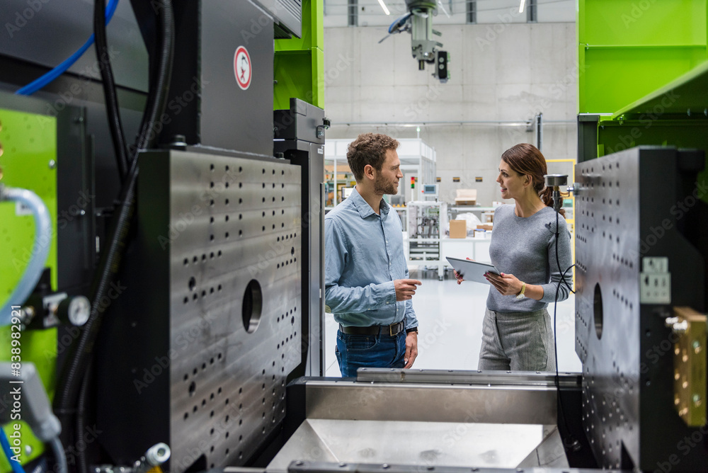 Colleagues in high tech company controlling manufacturing machines, using digital tablet