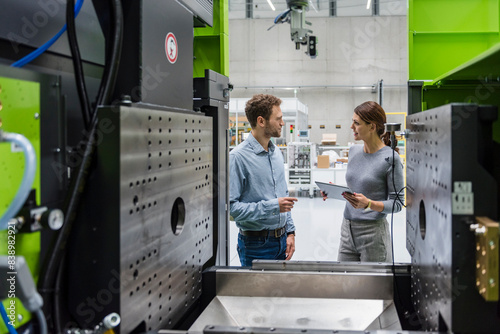 Colleagues in high tech company controlling manufacturing machines, using digital tablet