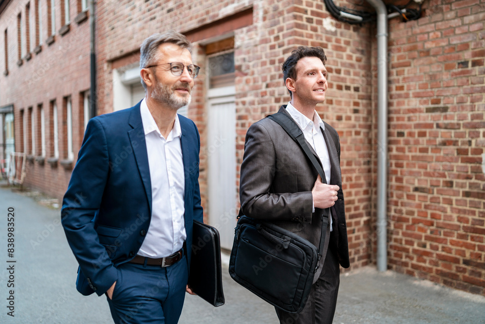Two smiling businessmen walking at an old brick building