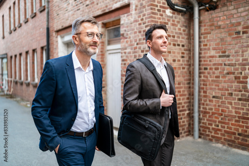 Obraz na płótnie Two smiling businessmen walking at an old brick building w salonie